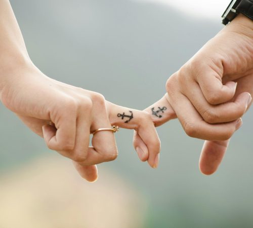 Close-up of a couple holding hands, featuring anchor tattoos symbolizing love and connection.